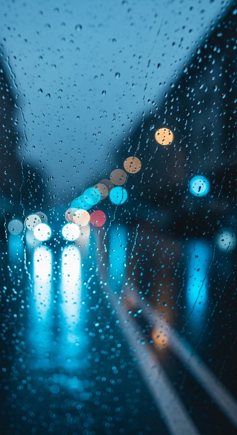 Raindrops on glass with blurred city traffic lights at night