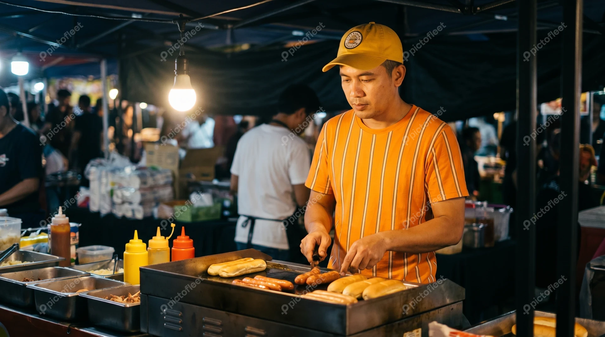 Man grilling hot dogs at a busy night market stall