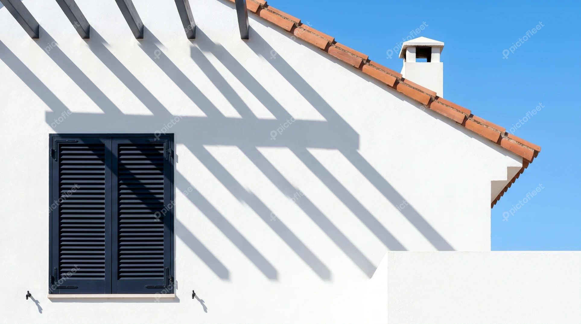 White Mediterranean facade with black window shutters and pergola shadows
