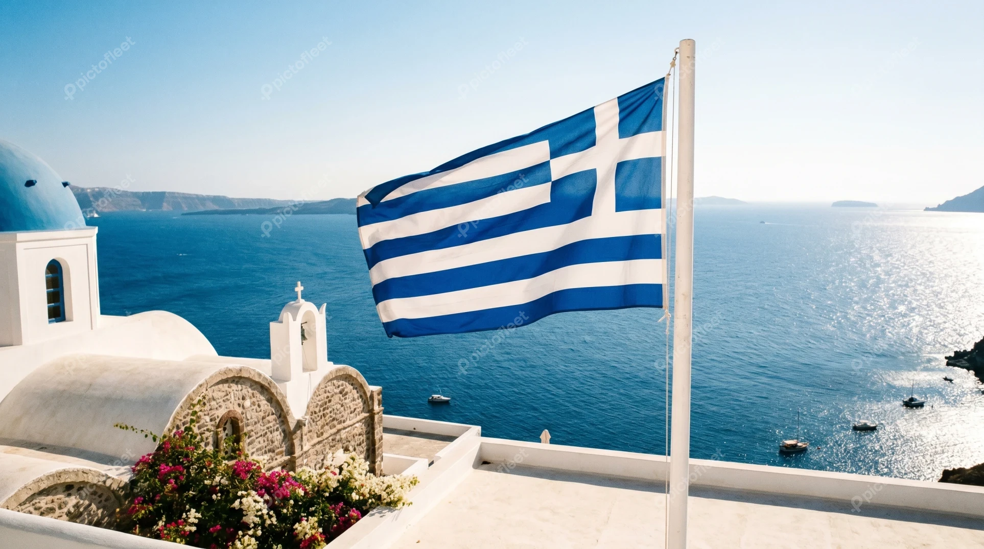 Greek flag waving over blue domed church in Santorini